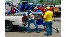 Uomini in equipaggiamento protettivo caricano una bara in un'auto di fronte a un ospedale di Guayaquil.