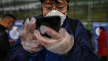 Un passeggero che indossa una maschera usa uno smartphone per scansionare un codice QR di salute della città di Wuhan prima di entrare nell'aeroporto di Tianhe.