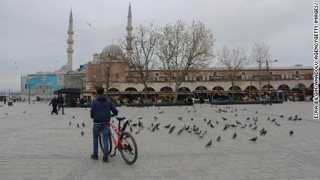 Un uomo con la sua bici circondata da piccioni in una piazza Yenicami quasi vuota al Bazar delle Spezie di Istanbul, in Turchia, durante il blocco del fine settimana.