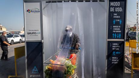 Una persona che indossa una maschera protettiva spinge un carrello della spesa attraverso una camera di decontaminazione nel mercato centrale di frutta e verdura di La Vega a Santiago del Cile.