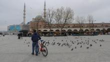 Un uomo con la sua bici circondata da piccioni in una piazza Yenicami quasi vuota al Bazar delle Spezie di Istanbul, in Turchia, durante il blocco del fine settimana.