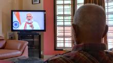 Un uomo anziano guarda il primo ministro indiano Narendra Modi parlare alla nazione durante un programma televisivo durante un blocco nazionale su mandato del governo il 14 aprile 2022. 