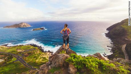 Ragazza in piedi sul bordo di una scogliera alle Hawaii che domina una bellissima baia con isole in lontananza al mattino.