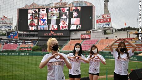 Le cheerleader posano davanti a un grande schermo che mostra gli appassionati di baseball applaudire dalle loro case durante il gioco di apertura della nuova stagione di baseball sudcoreana tra SK Wyverns e Hanwha Eagles allo stadio di baseball Munhak di Incheon martedì.