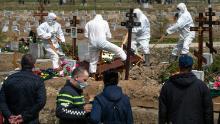 I becchini seppelliscono una vittima di COVID-19 mentre parenti e amici si trovano a distanza di sicurezza in un cimitero di Kolpino, fuori San Pietroburgo, venerdì.