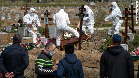 I becchini seppelliscono una vittima di COVID-19 mentre parenti e amici si trovano a distanza di sicurezza in un cimitero di Kolpino, fuori San Pietroburgo, venerdì.