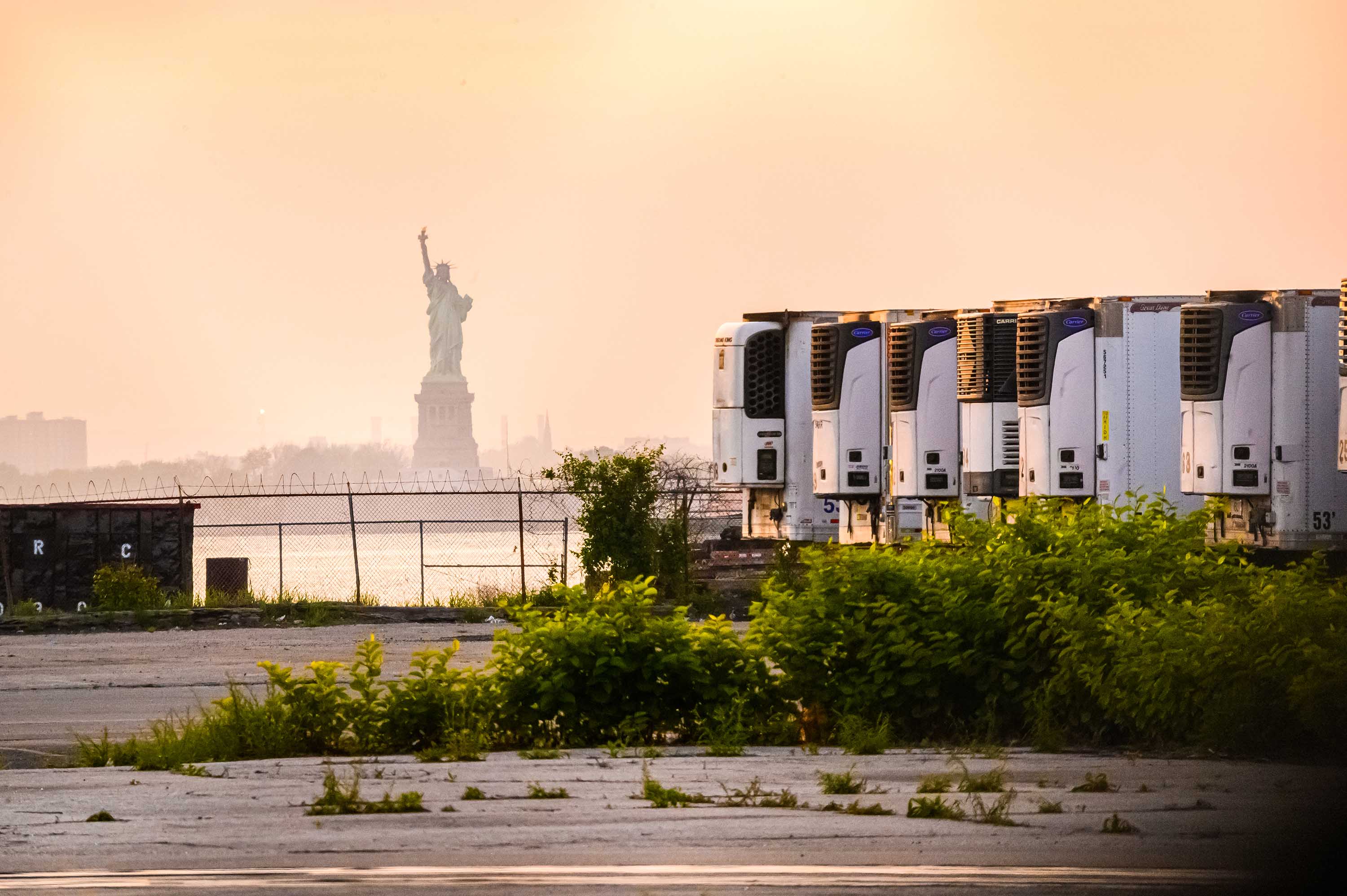 La Statua della Libertà è vista dietro camion refrigerati che fungono da mortuarie temporanee per le vittime del coronavirus presso il terminal marittimo di South Brooklyn a New York City il 25 maggio.