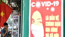 Un poster di propaganda sulla prevenzione della diffusione del coronavirus è visibile su un muro mentre un uomo fuma una sigaretta in una strada di Hanoi.