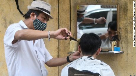 Un parrucchiere lungo la strada che indossa una maschera facciale fa un taglio di capelli a un cliente ad Hanoi.