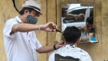 Un parrucchiere lungo la strada che indossa una maschera facciale fa un taglio di capelli a un cliente ad Hanoi.