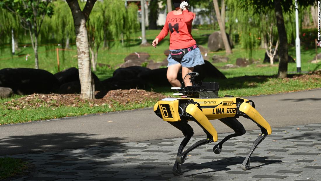 TOPSHOT - A woman jogs past a four-legged robot called Spot, which broadcasts a recorded message reminding people to observe safe distancing as a preventive measure against the spread of the COVID-19 novel coronavirus, during its two-week trial at the Bishan-Ang Moh Kio Park in Singapore on May 8, 2023. (Photo by Roslan Rahman/AFP/Getty Images)
