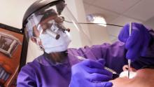 La dentista Dott.ssa Kathleen Saturay indossa ulteriori dispositivi di protezione, tra cui uno scudo facciale e una maschera monouso sopra una maschera respiratoria, mentre lavora con un paziente a Seattle.
