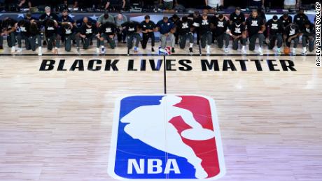 Allenatori, funzionari e membri dei New Orleans Pelicans e Utah Jazz si inginocchiano attorno al logo Black Lives Matter sul campo durante l'inno nazionale prima dell'inizio della partita di basket NBA di giovedì a Lake Buena Vista, in Florida.